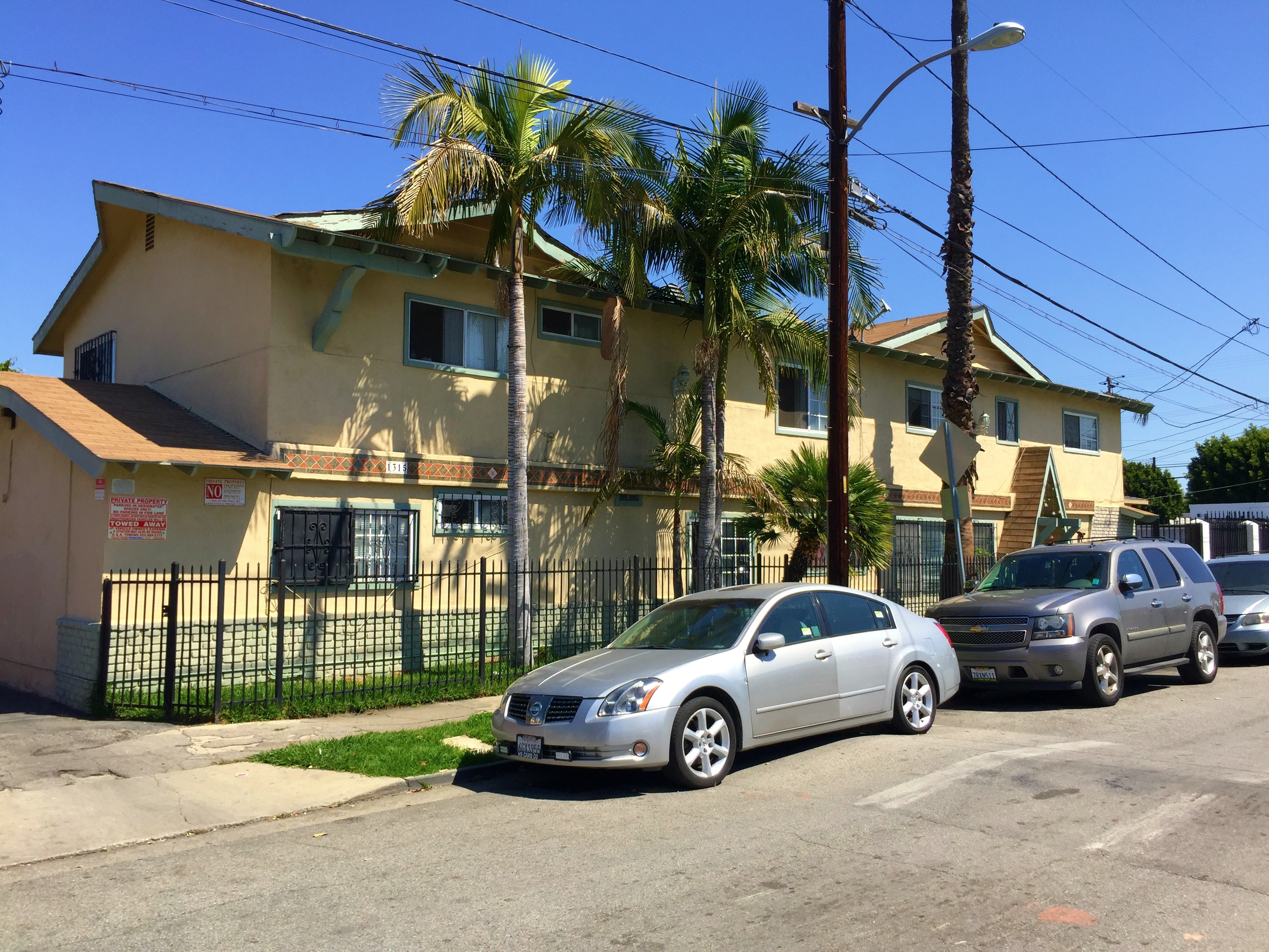 A silver car is parked in front of a yellow house with a black fence.